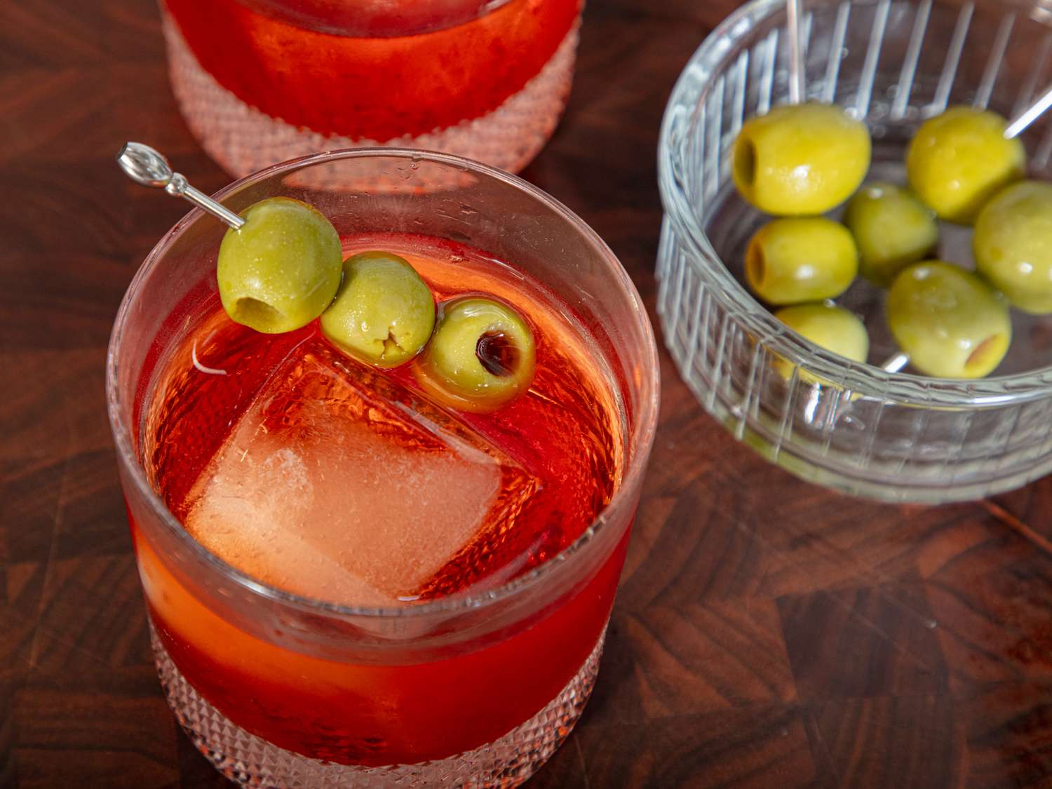 A Negroni cocktail with skewered olives served in a glass with ice