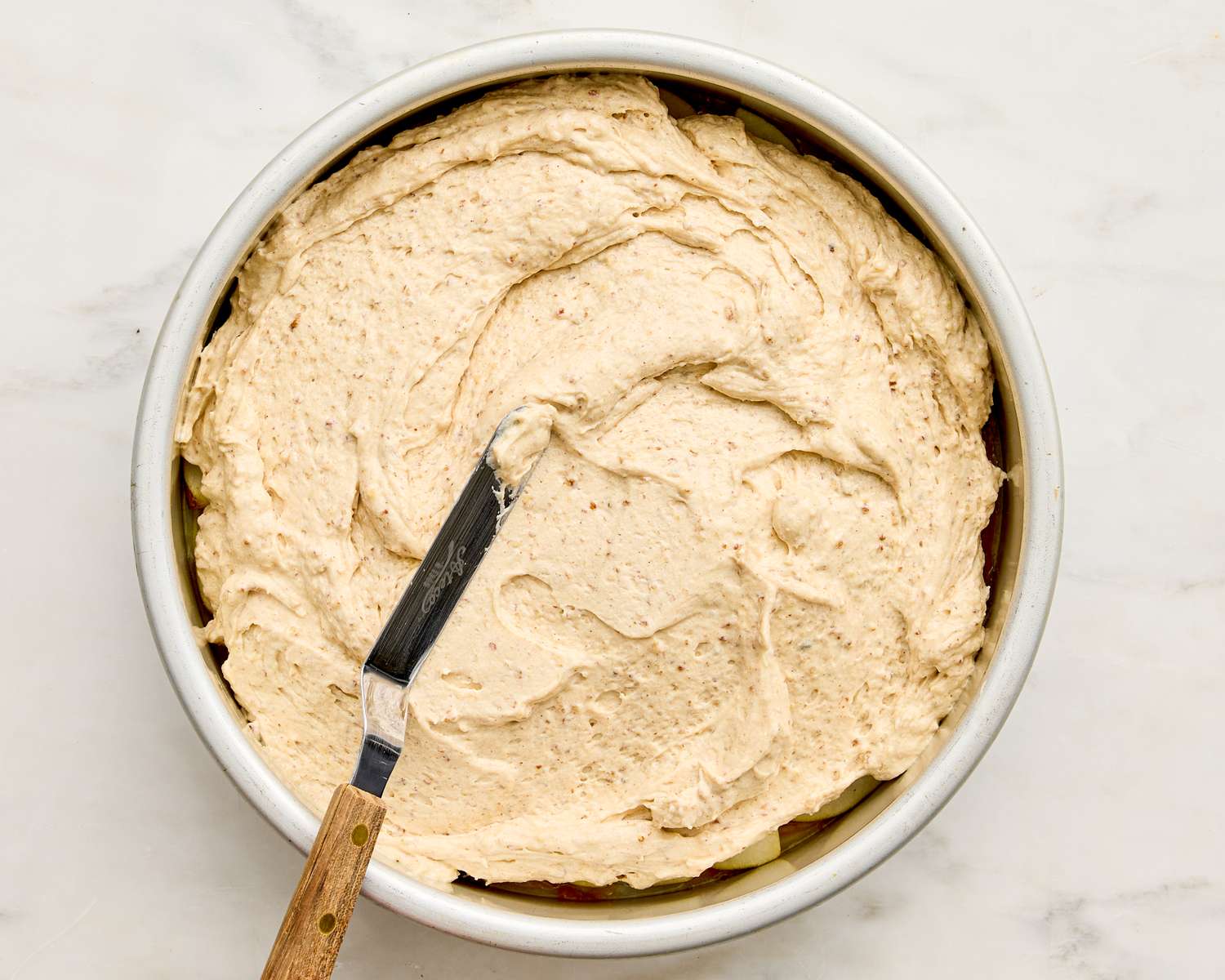 Cake batter spread in a round pan with an icing spatula resting on top