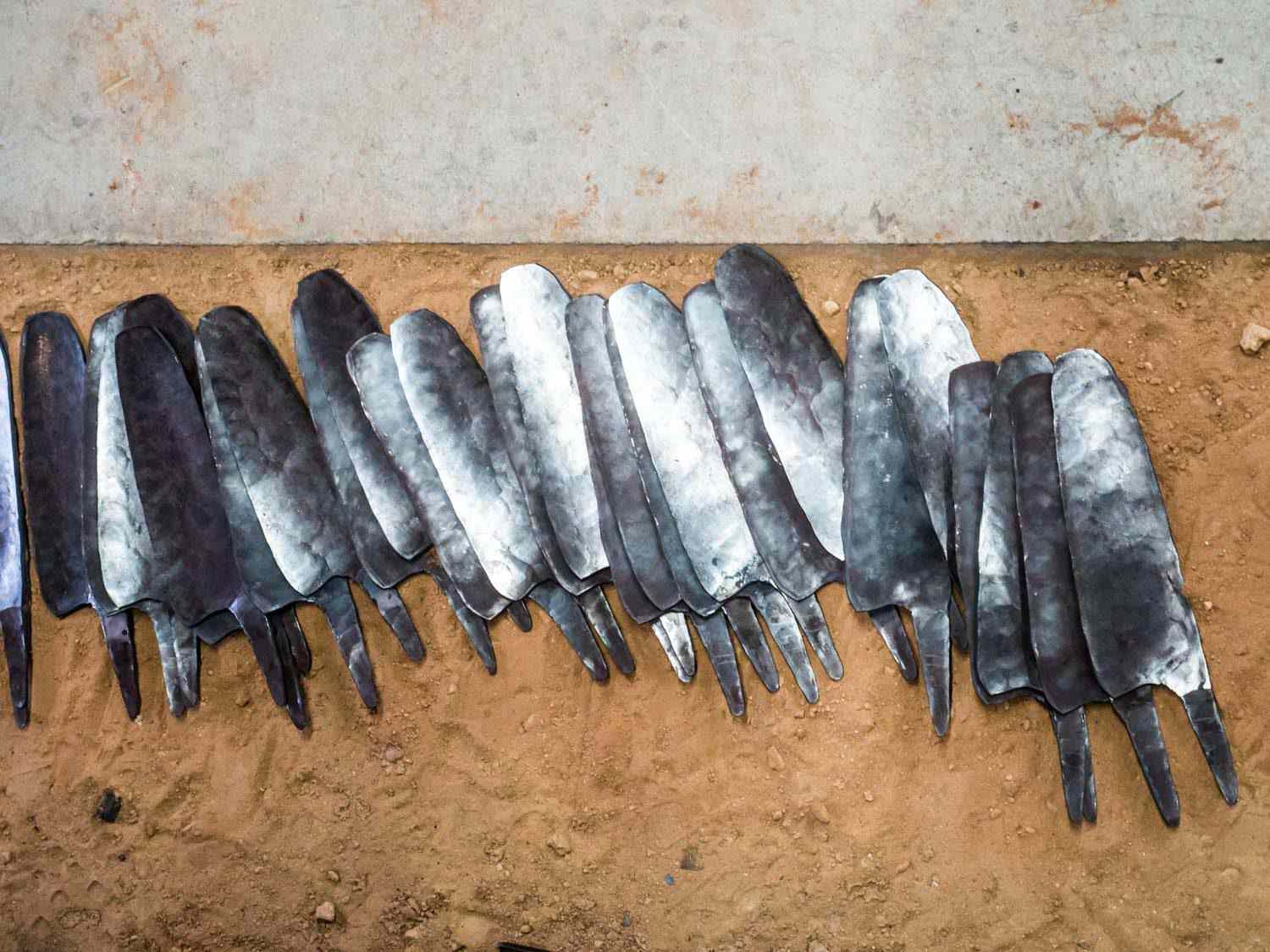 Two dozen knife blanks are arrayed on the floor.