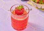 A glass of strawberry smash cocktail with a whole strawberry garnish