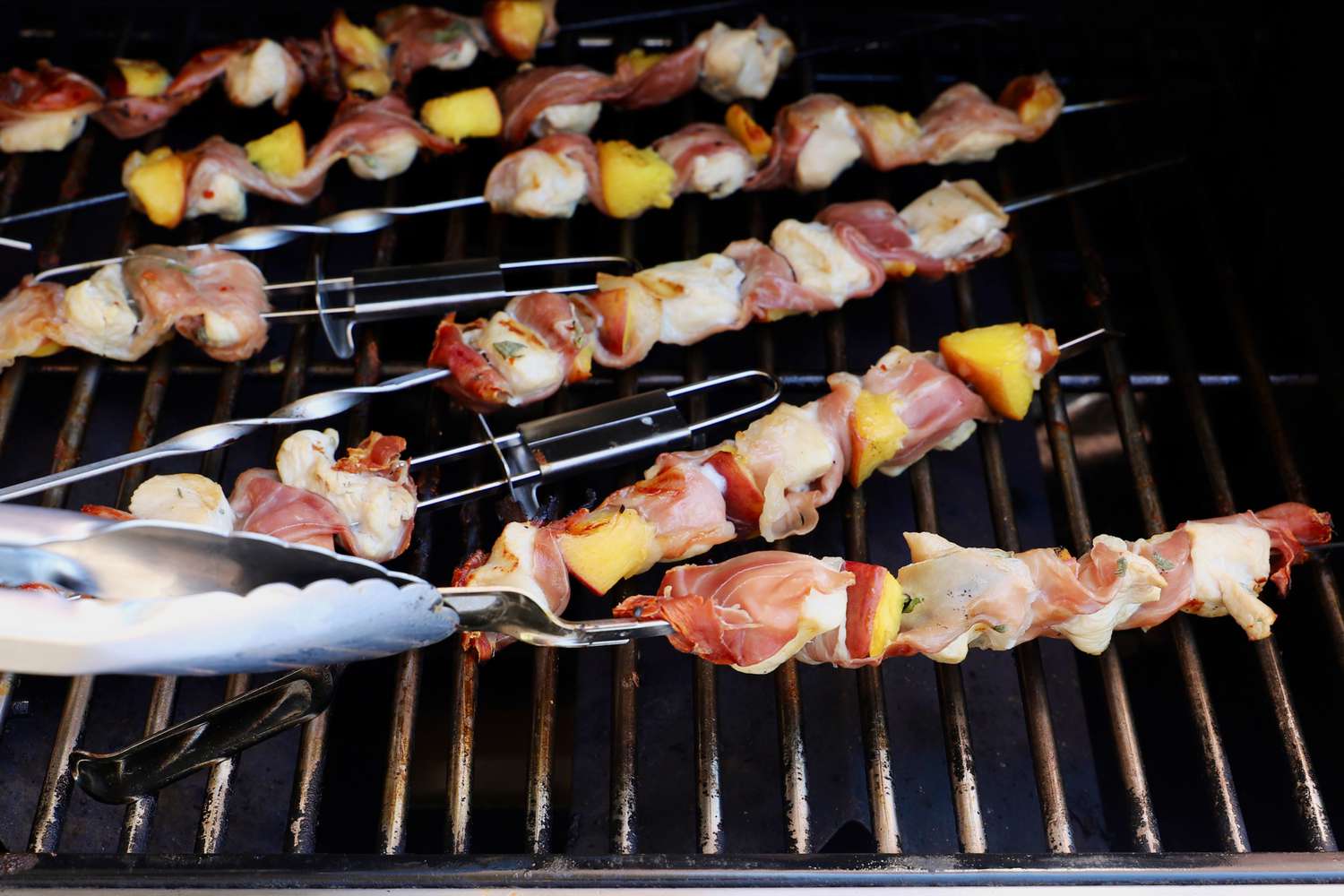 A person flipping a stainless steel skewer on a grill.