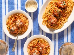 Plates of spaghetti with chicken parmesan meatballs on a blue striped tablecloth