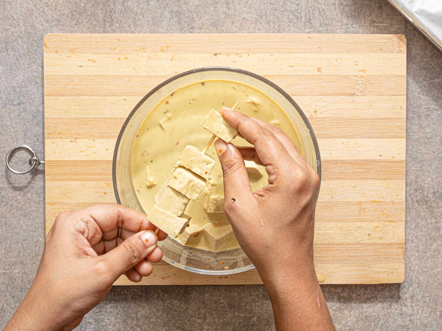 Person dipping tofu cubes into a yellow marinade placed on a wooden cutting board