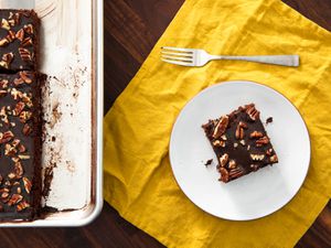 Overhead view of a slice of Texas sheet cake served on a white plate and set next to the rest of the cake.