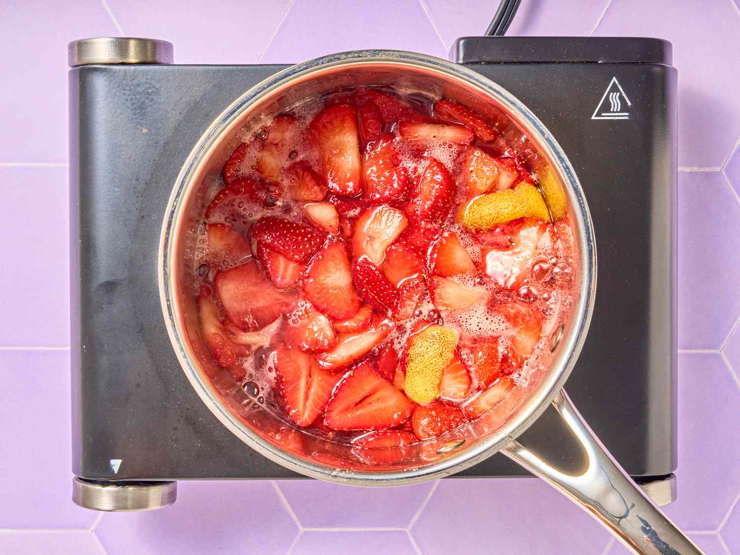 Strawberries and lemon peel cooking on a stovetop in a pot