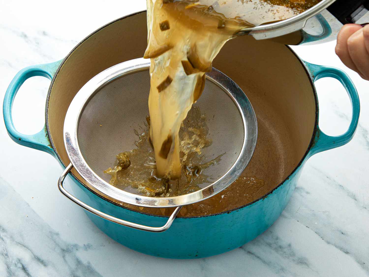 Pouring broth through a sieve in a dutch oven 