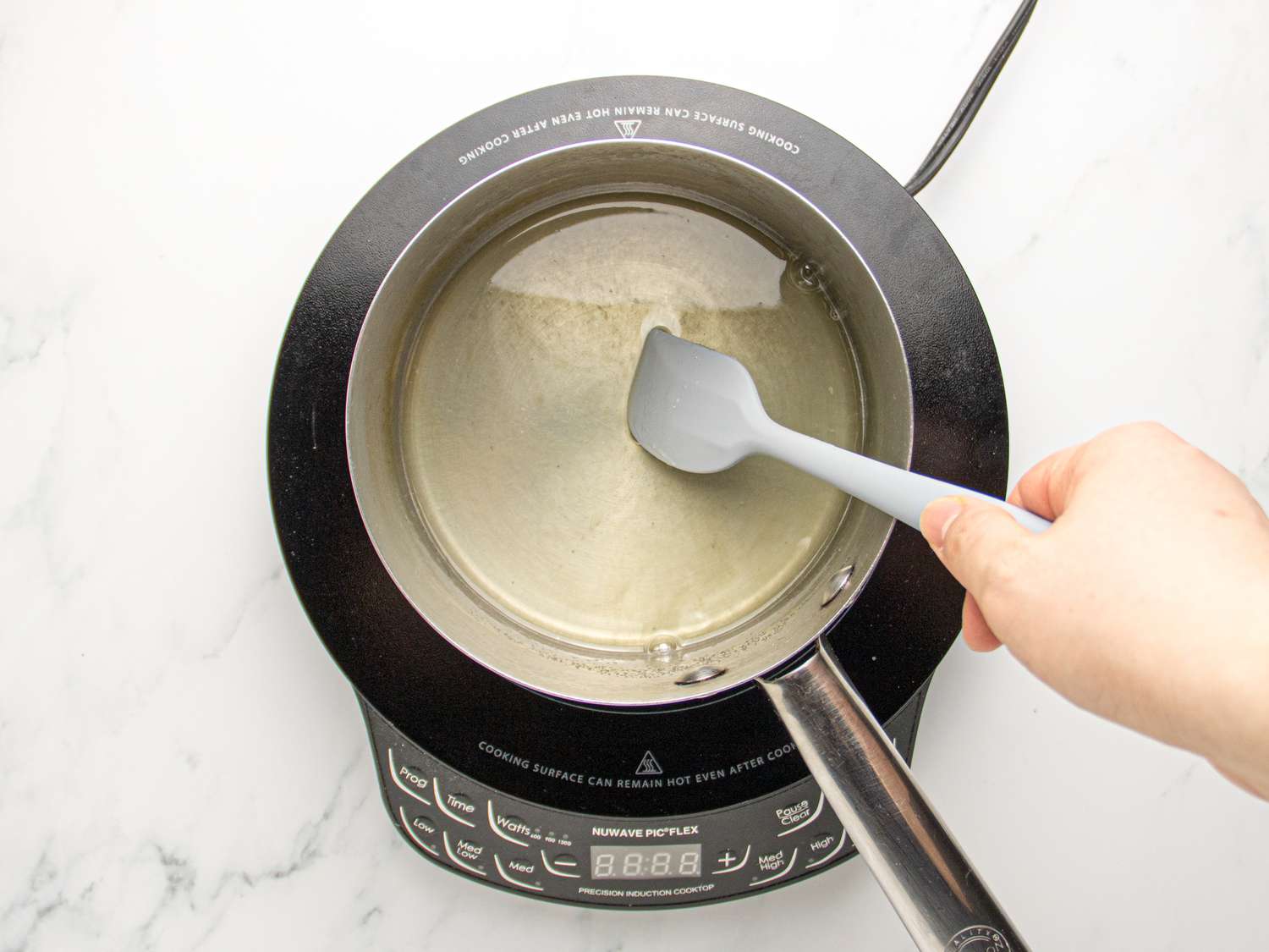 Hand stirring batter with a spatula in a saucepan on an induction cooktop.