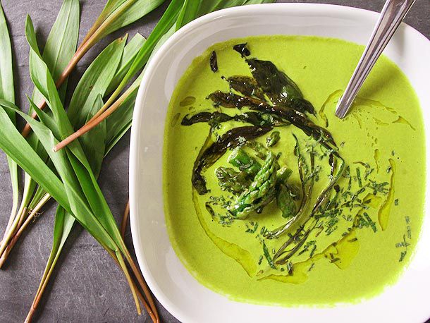 Overhead view of Asparagus and Ramp Soup With Yogurt, served in a white squarish bowl with ramp greens scattered to one side.