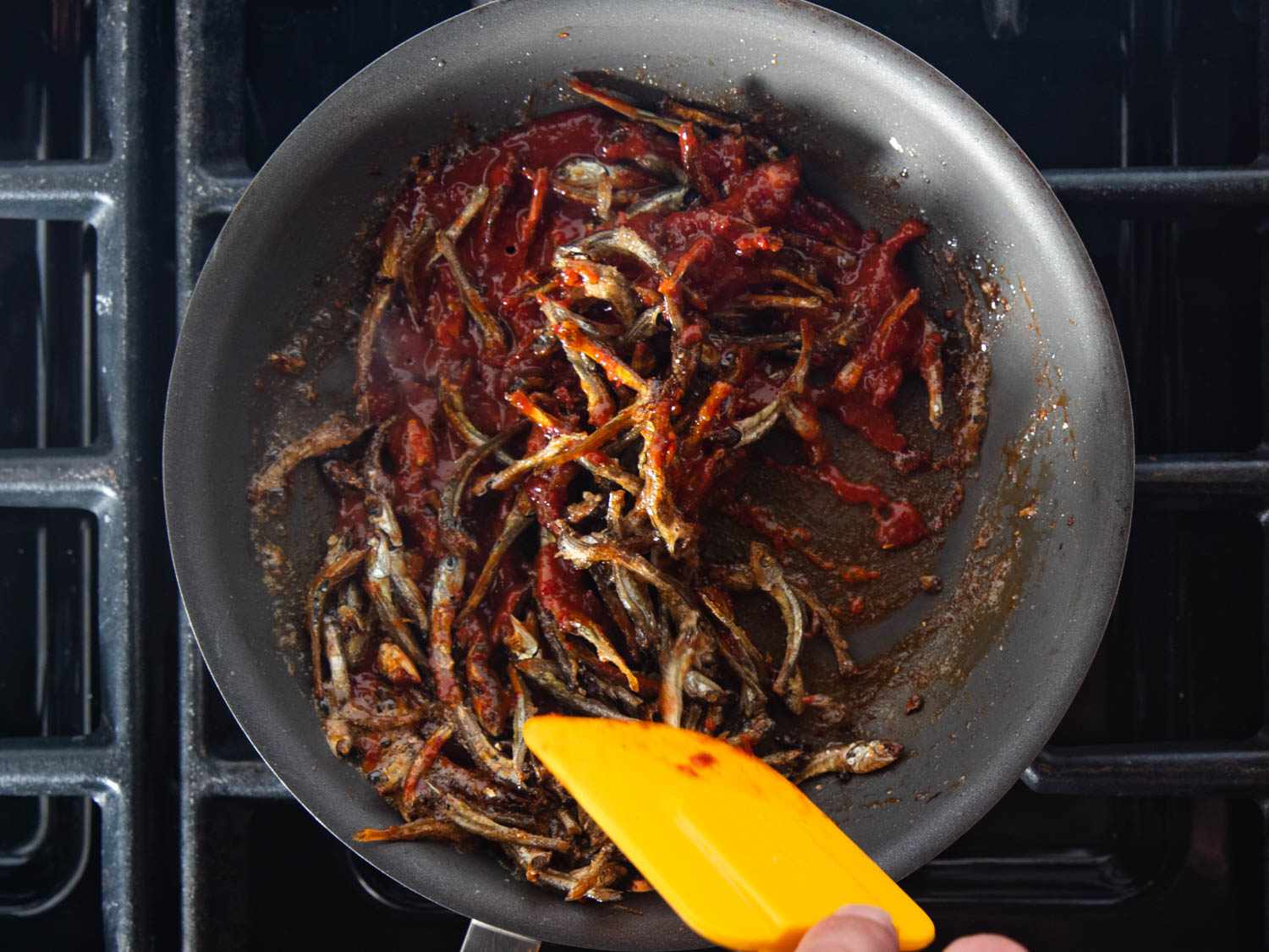 The anchovies are stirred and cooked until glazed with the gochujang mixture.