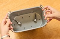 Two hands holding the Zojirushi Home Bakery Virtuoso Plus Bread Maker basket over wood