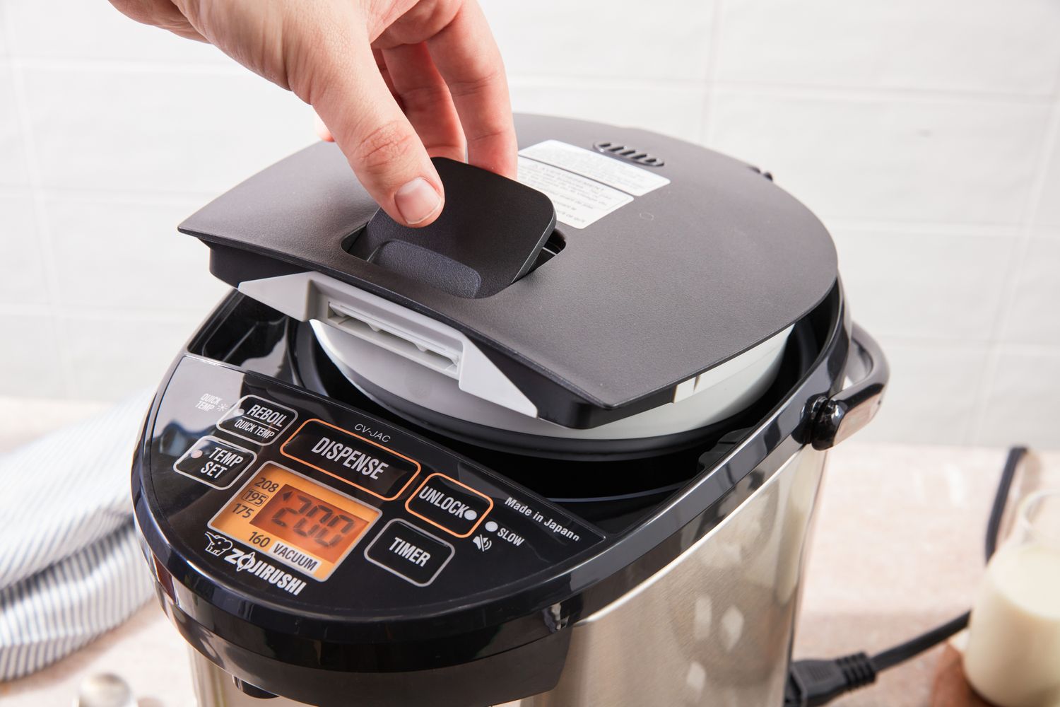A hand lifting a lid on a modern electric appliance with buttons and display