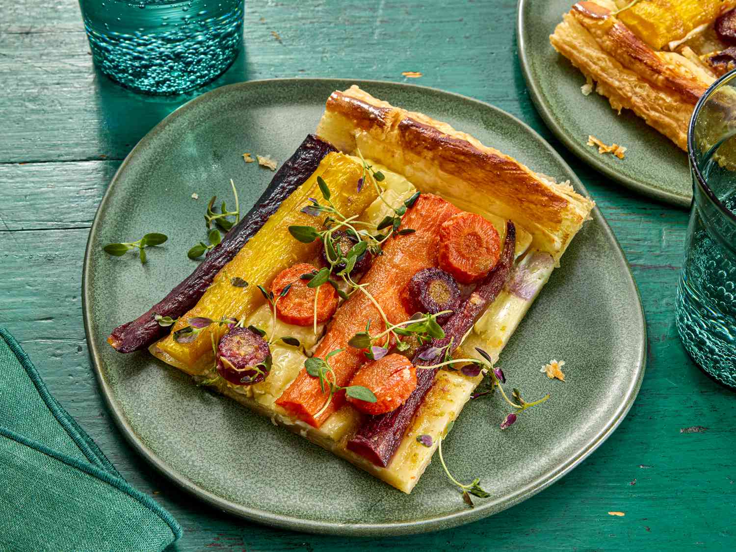 square of carrot tart on green plate, with green wooden surface and green glass of sparkling water 