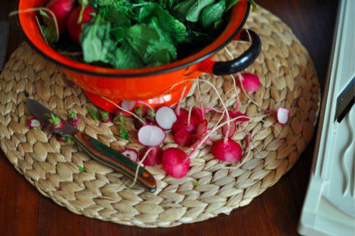 Sliced radish tops next to a bowl of whole radishes.