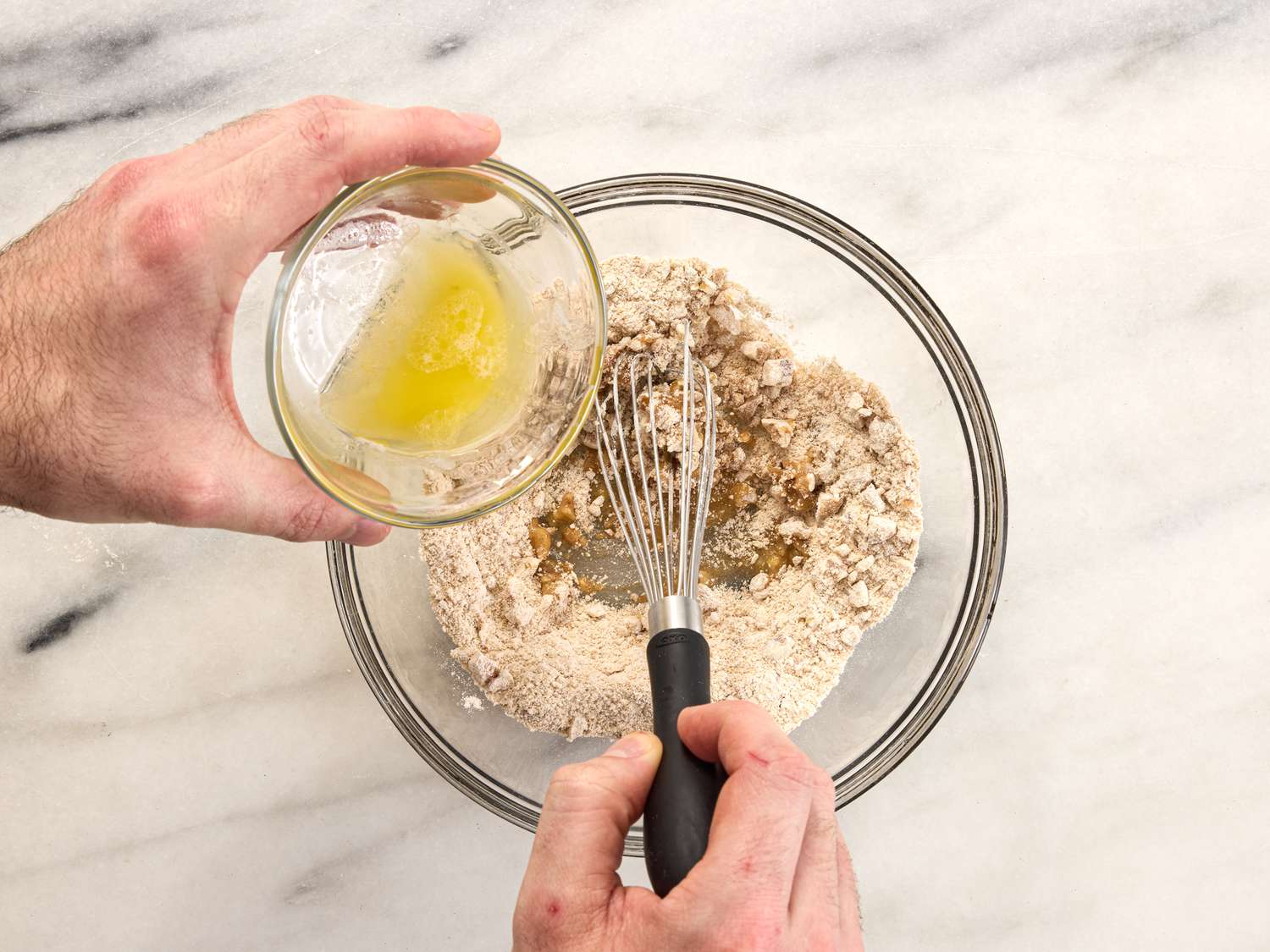 adding butter into mixture on bowl with whisk in glass bowl