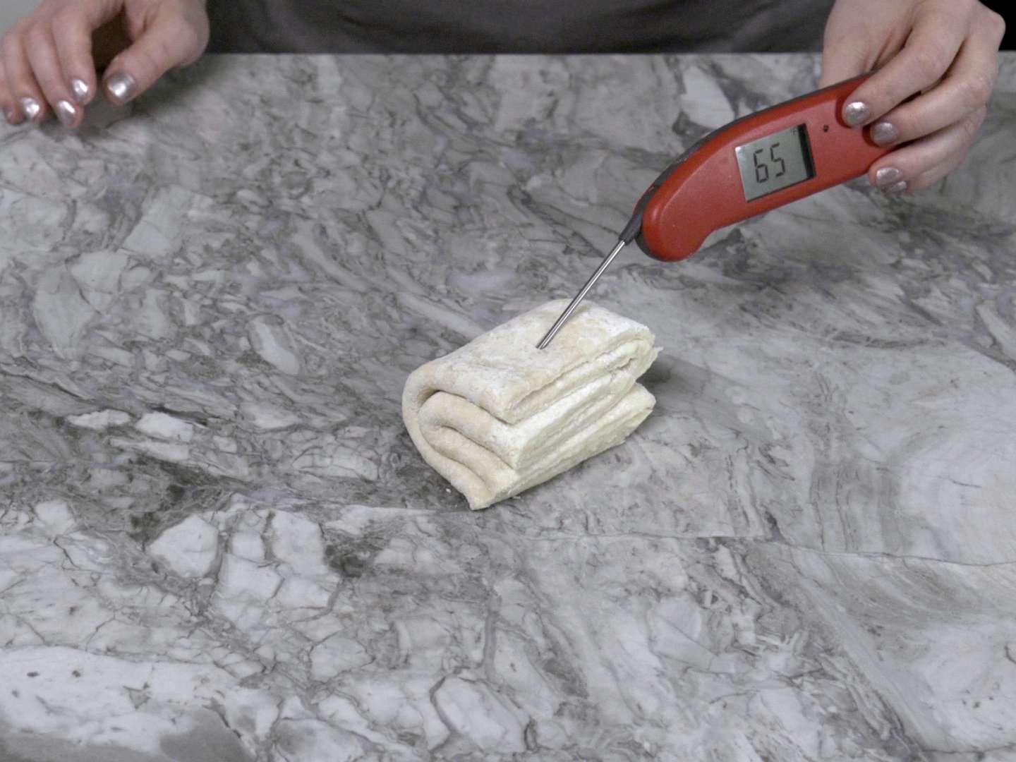 A thermometer inserted into a stack of folded pie dough, registering 65 degrees Fahrenheit
