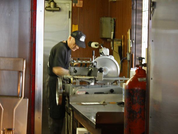 A line cook in the kitchen of Al's, manning a meat slicer.