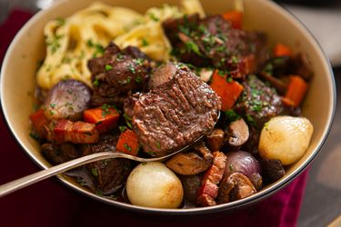 A bowl of beef stew with vegetables and garnished herbs