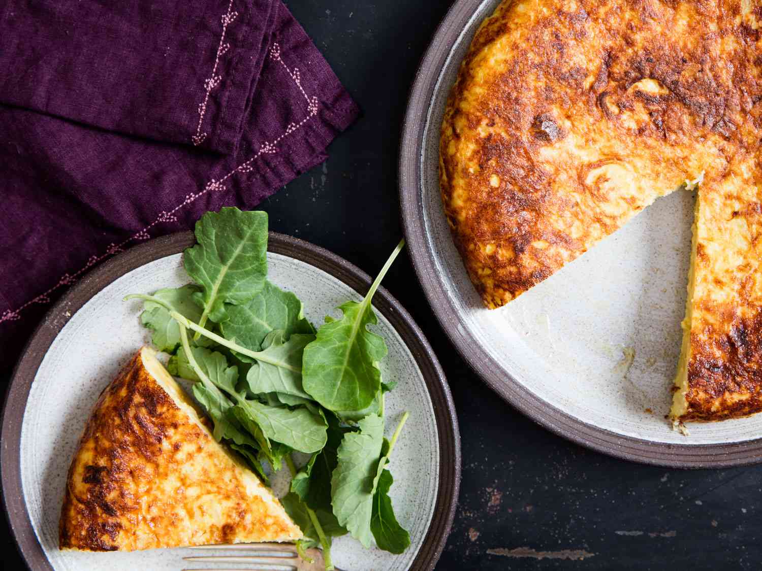 Tortilla española on a plate, with a slice removed and presented on another plate with some unadorned greens.
