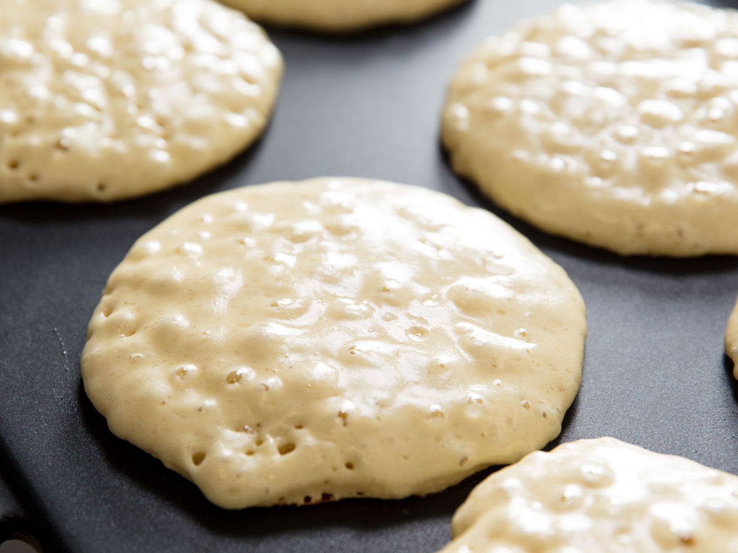 Close up of pancake batter being cooked on a griddle. The surface of the batter begins to bubble. 