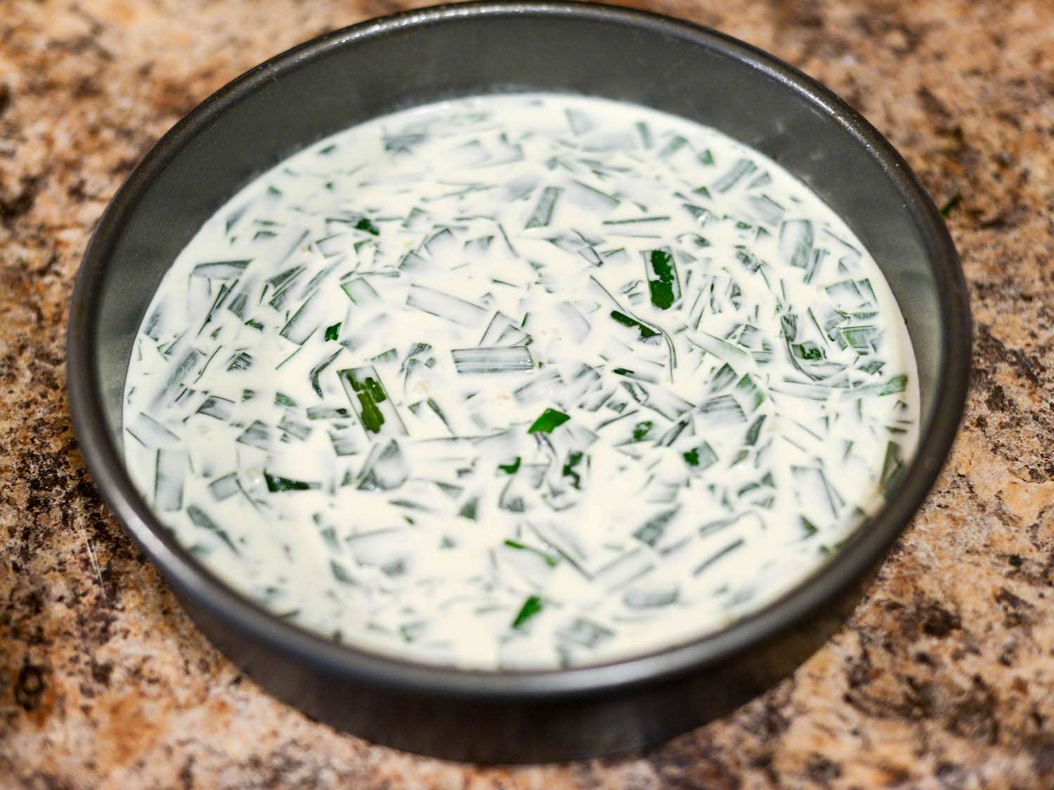 Sticky rice cake batter with chopped Chinese chives in a round cake pan.