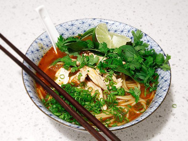  A bowl of Thai Red Curry Noodle Soup With Chicken, with soup spoon and chopsticks.