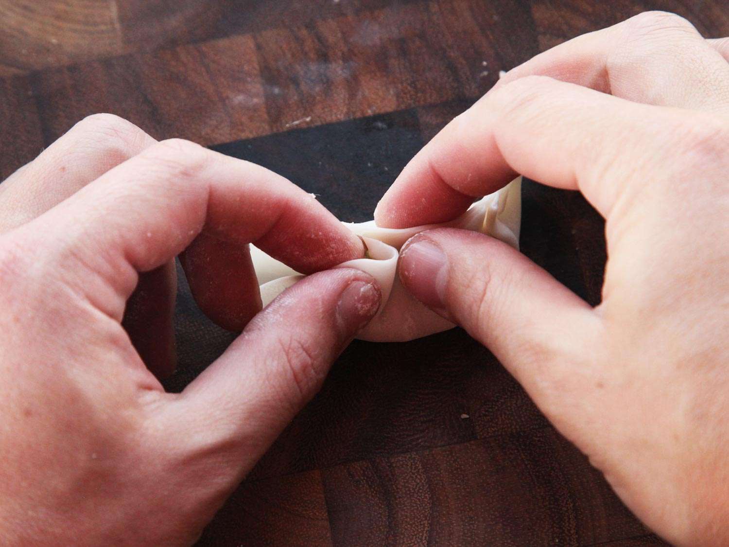 Using both hands to fold pleats in the top of a dumpling to form gyoza. 