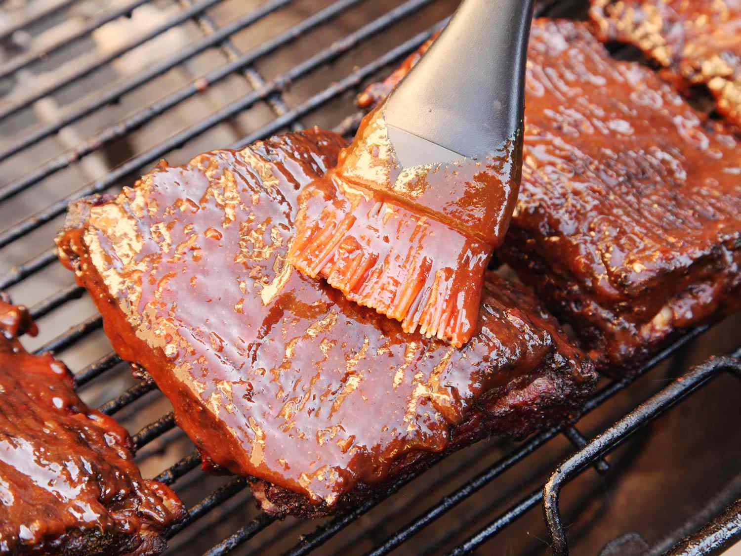 Barbecue sauce being brushed onto ribs on a grill