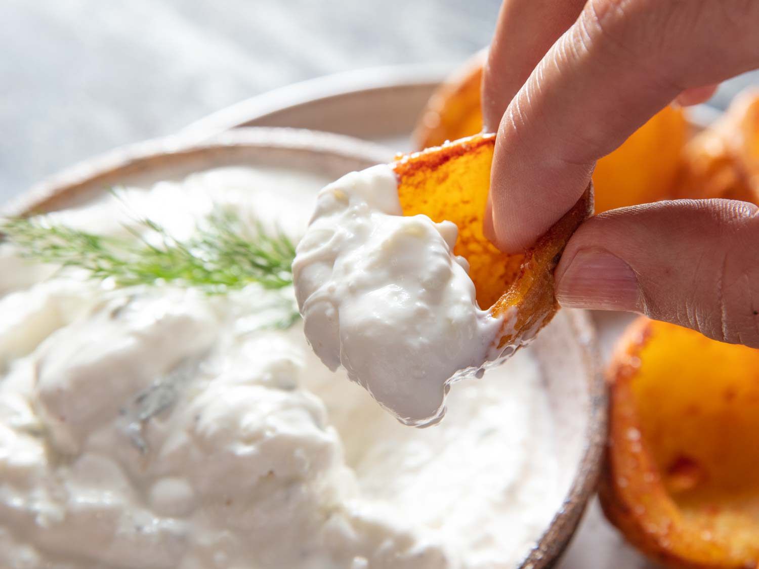 Dipping a deep-fried potato skin cup into a bowl of tzatziki