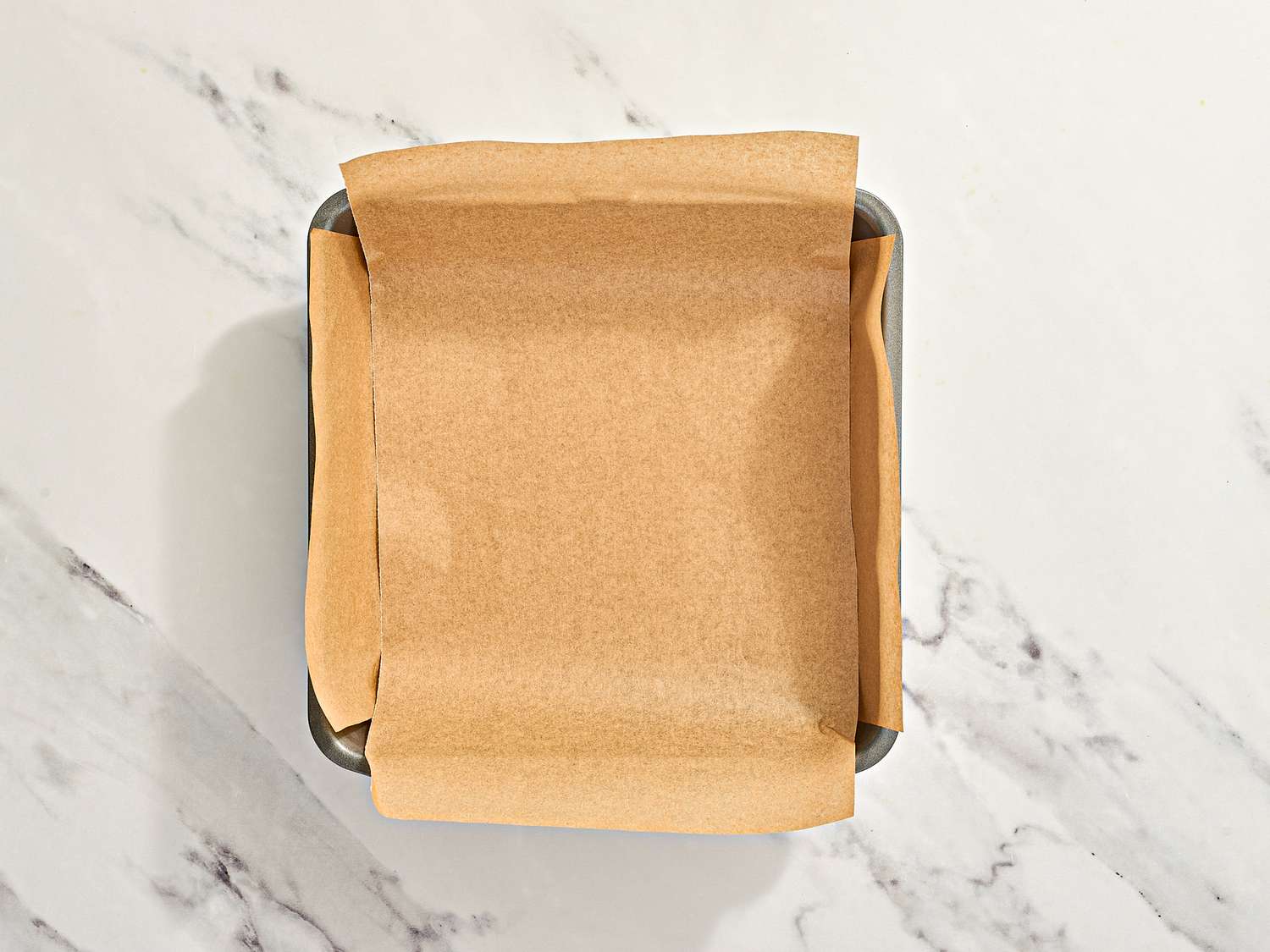 Parchment paper lining a square baking pan on a marble countertop