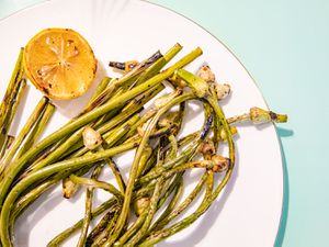 Grilled Garlic scapes on a white plate with a lemon 
