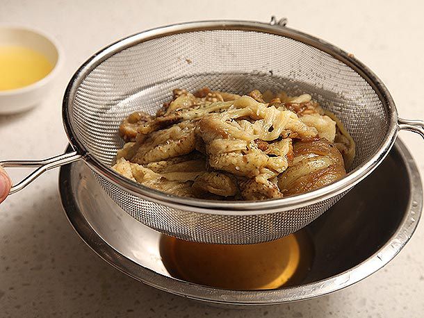Cooked eggplant flesh in a metal strainer held over a bowl