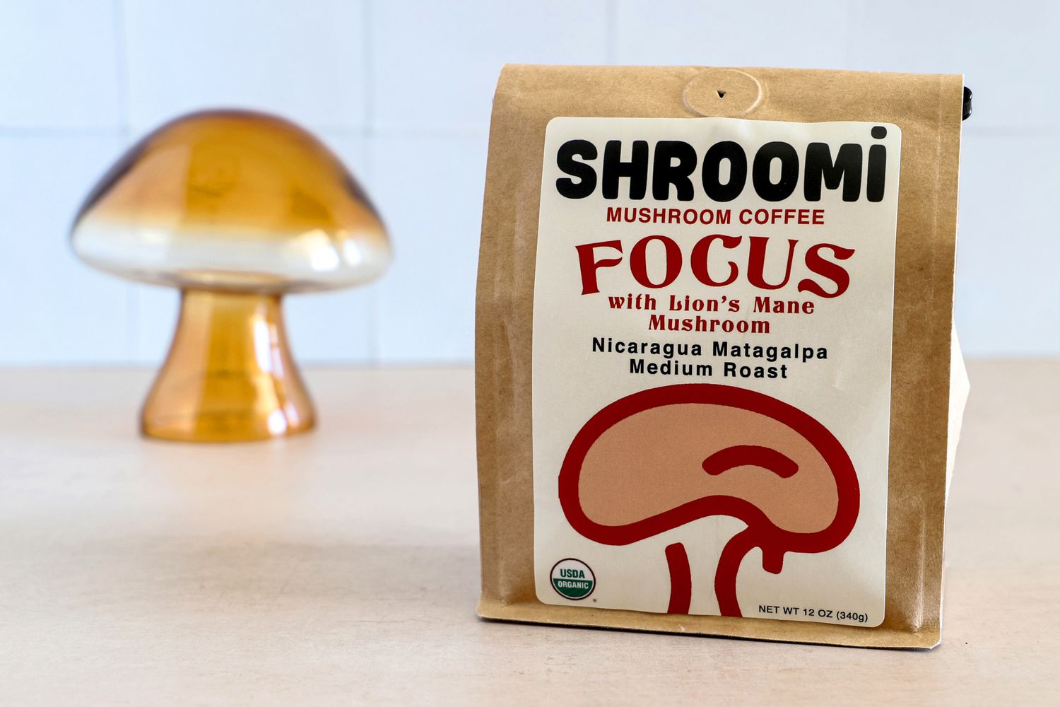 A package of Shroomi mushroom coffee with a golden glass object in the background, on a wooden surface
