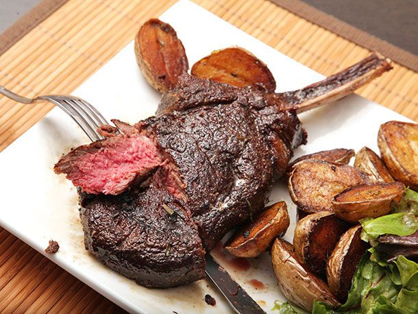 Forkful of medium rare steak cut from bone-in browned bison ribeye steak plated with crispy potatoes 