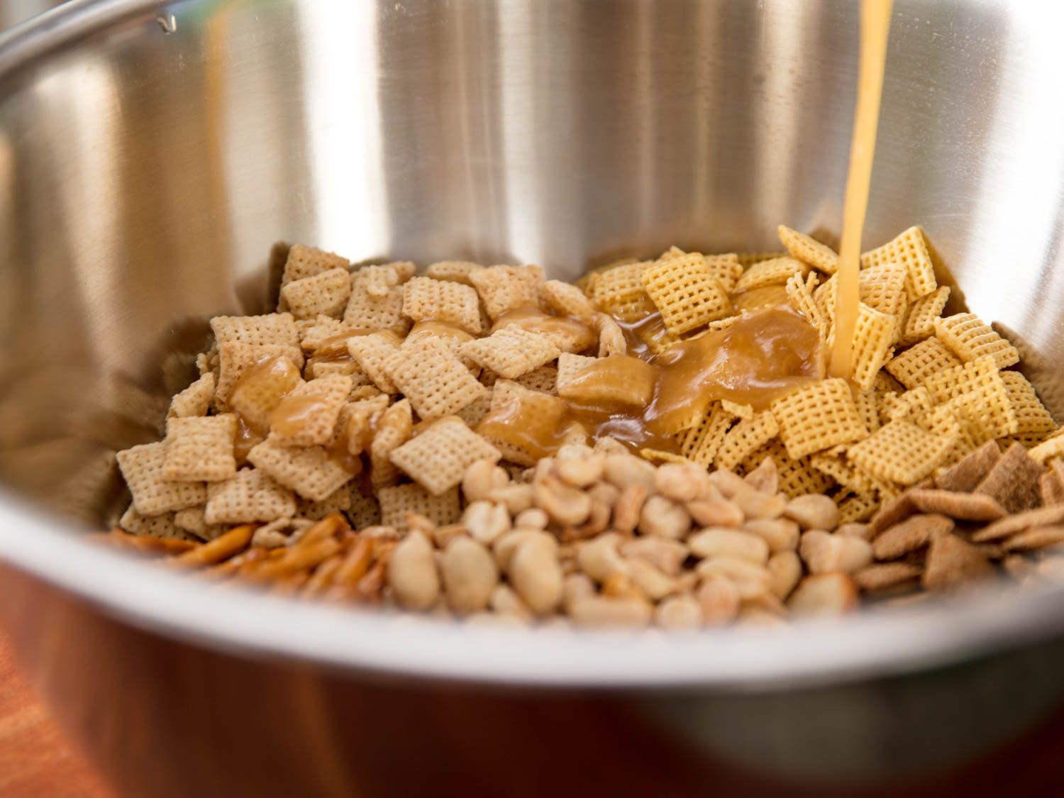 Butter mixture being poured into the bowl of chex mix ingredients.