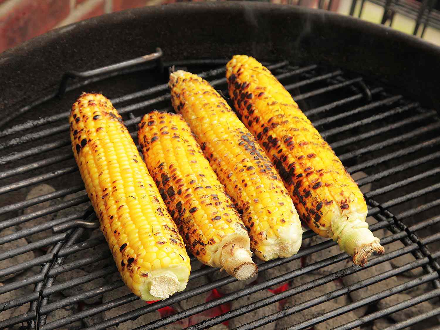 Four ears of corn grilling over charcoal