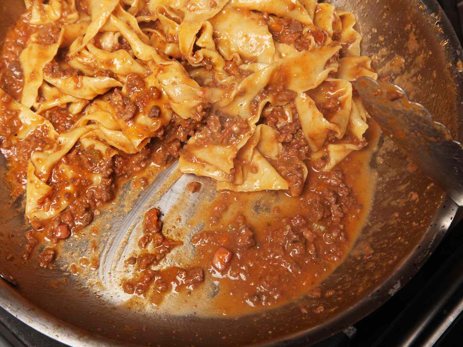 Sauced tagliatelle in a wide pan. Pasta cooking water has been added and the tagliatelle and sauce look glossy.