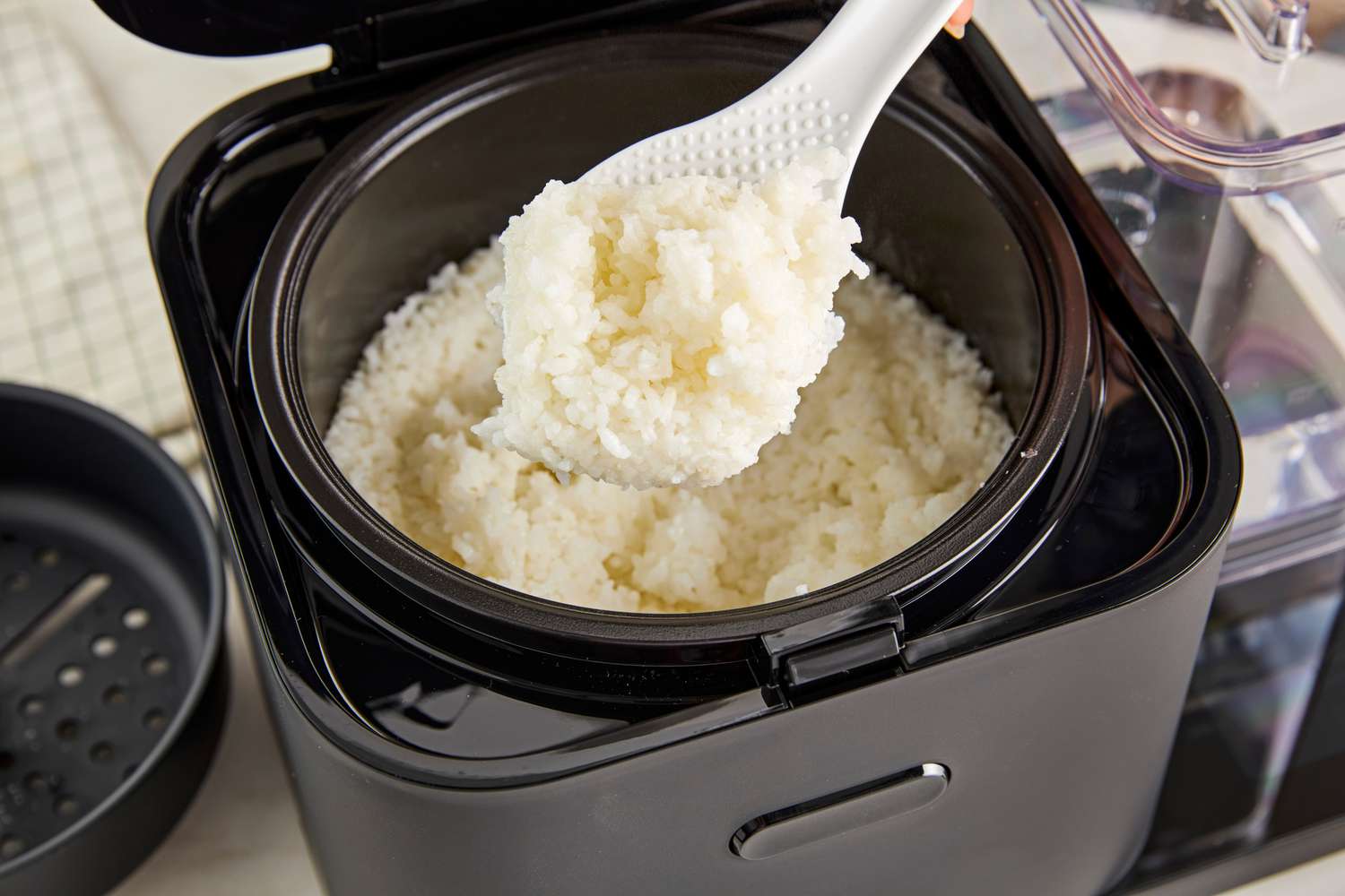 Cooked rice being scooped out of the KitchenAid rice cooker.