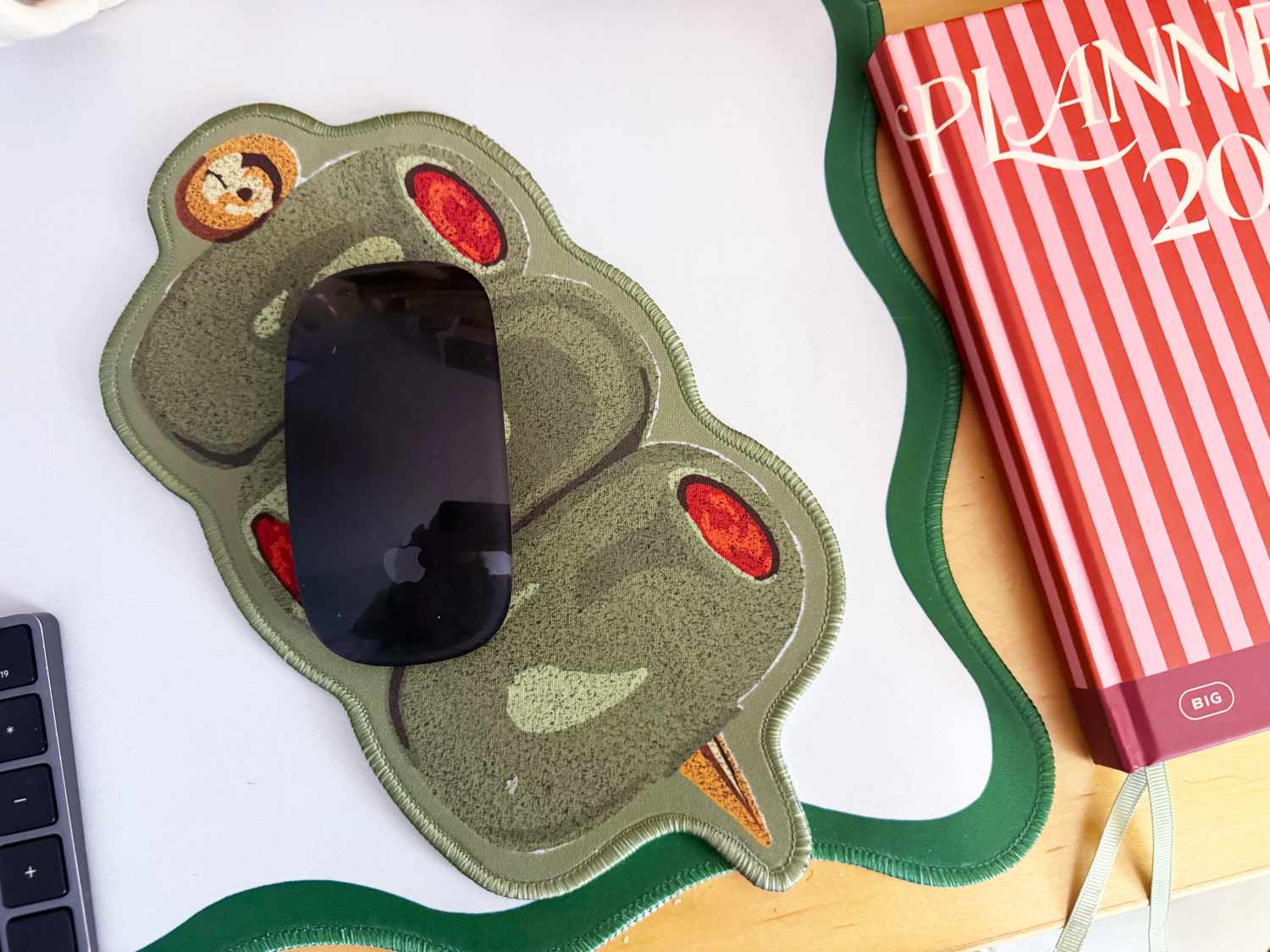 Novelty olivethemed mouse pad with a design of green olives stuffed with red pimentos placed on a desk next to a planner and keyboard