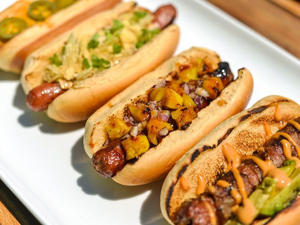 Four hot dogs in buns arranged on a white platter, each topped with a different combination of condiments.