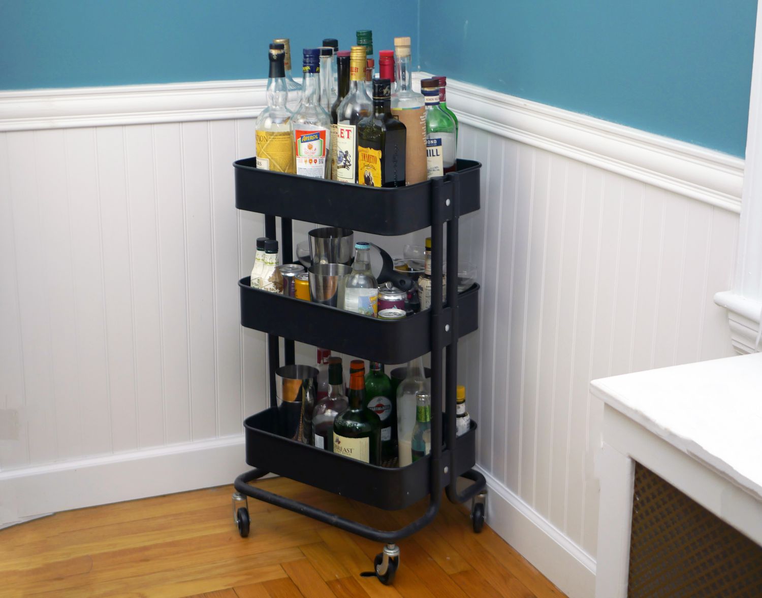 A utility cart with three shelves loaded with liquor bottles.