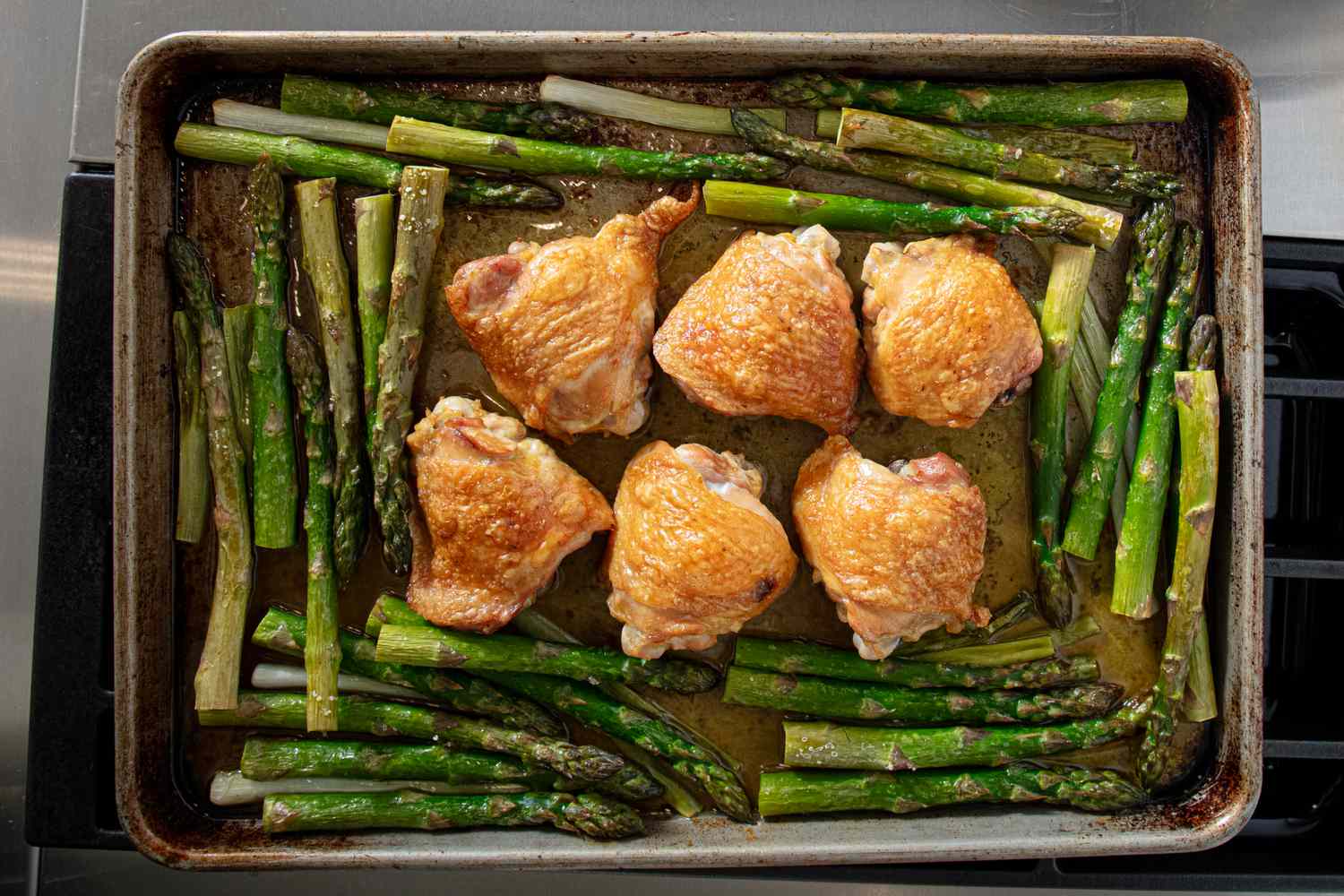 Roasted chicken thighs with asparagus on a baking sheet, a meal preparation step