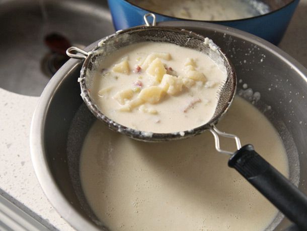 Straining out cooked clams and potatoes over a metal bowl.