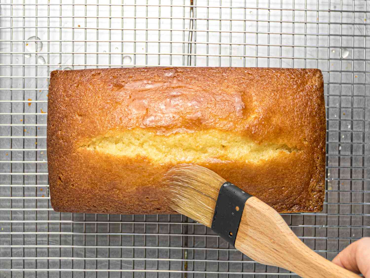Lemon pound cake on a cooling rack being brushed with syrup.