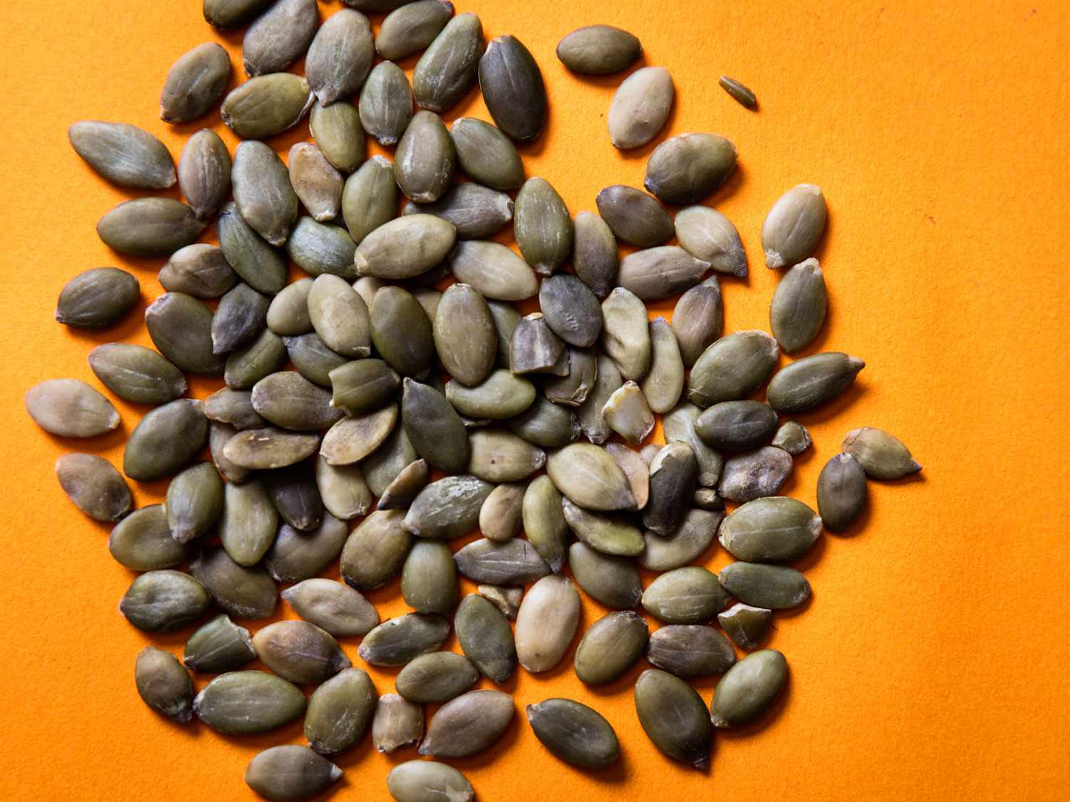 Close-up of a pile of pepitas (pumpkin seeds) against an orange background