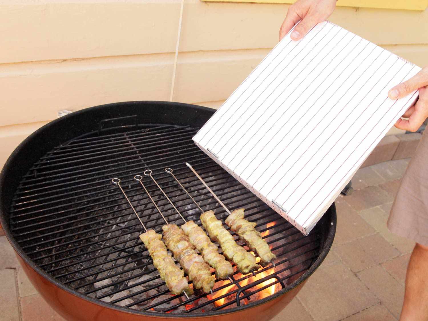 Fanning skewered meat on the grill using a cardboard box top.