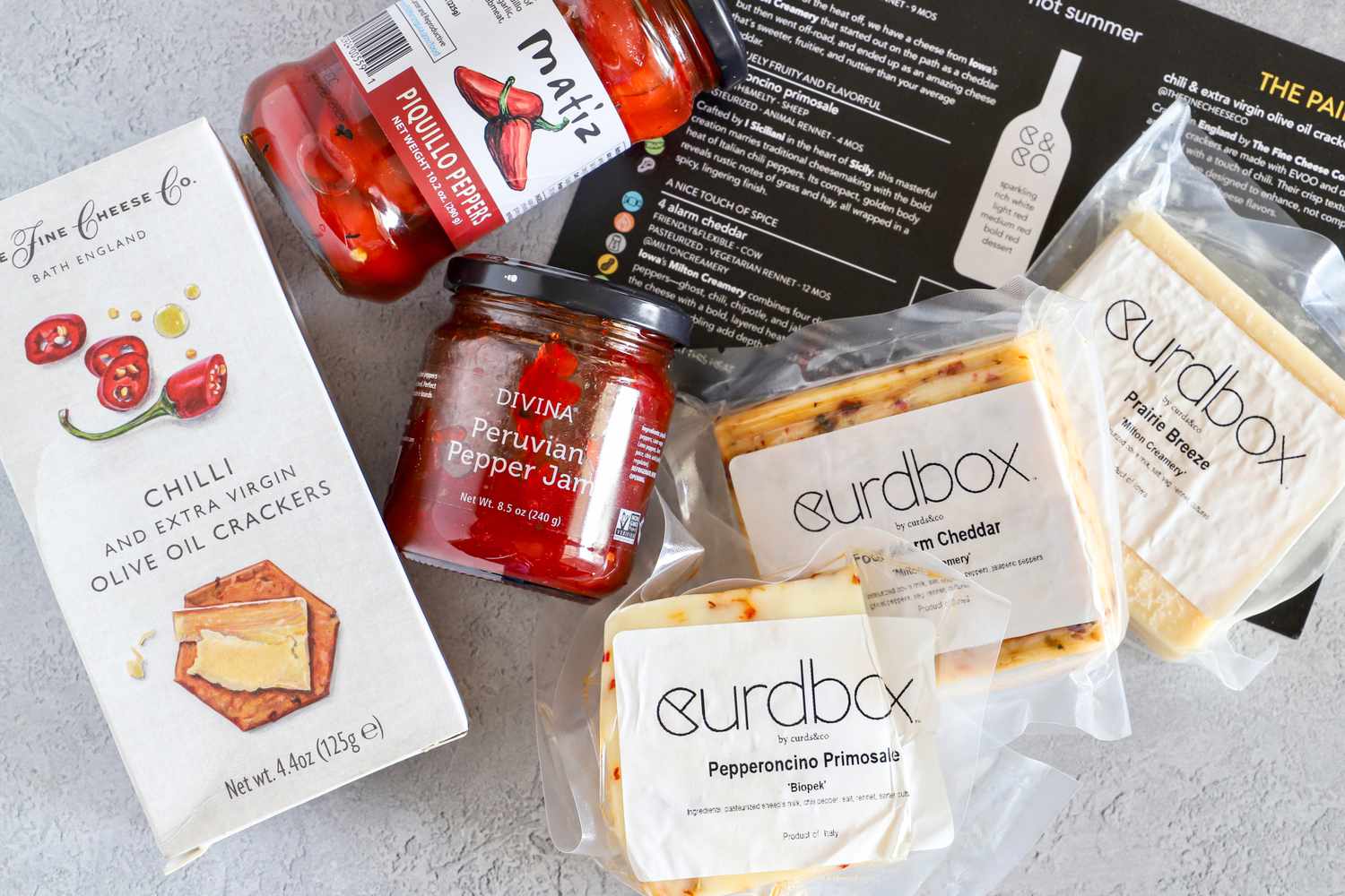 Various gourmet food items from Curdbox Cheese Subscription Box, including crackers pepper jam and cheese with labels visible from brands