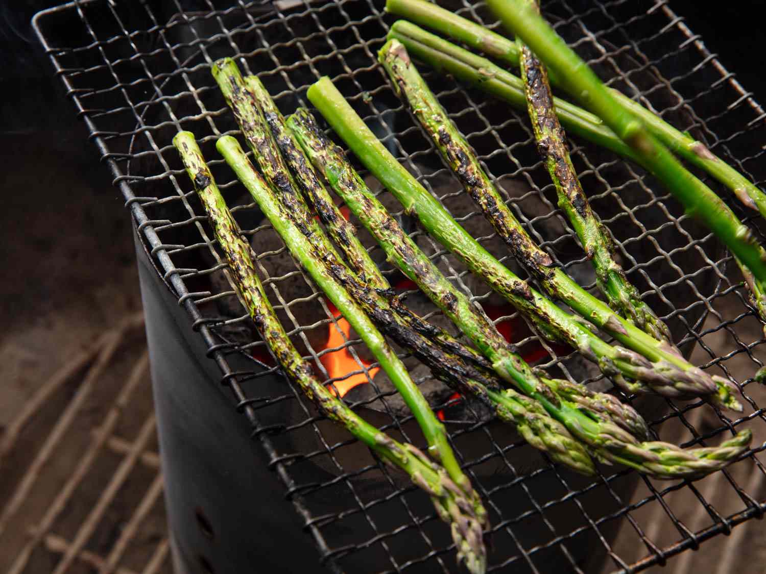 Asparagus spears getting nicely charred, suspended with a metal rack over a charcoal chimney.