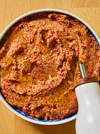 A bowl filled with muhammara topped with olive oil on a wooden surface