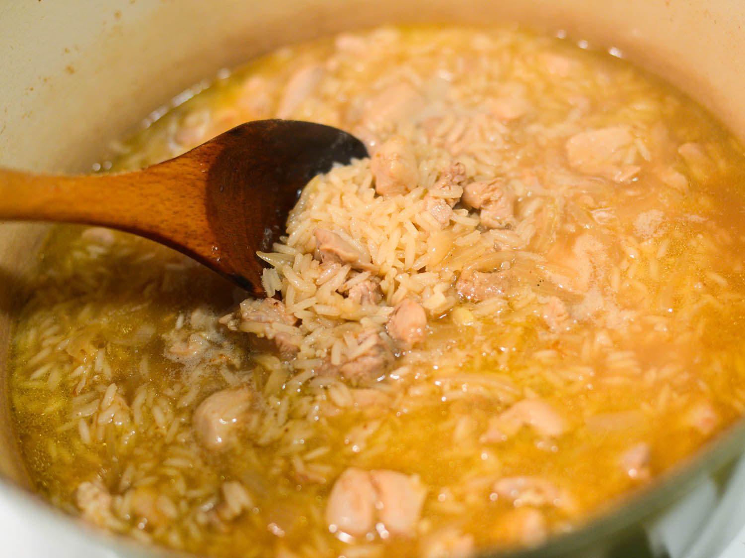 Author stirring the arroz caldo midway through cooking. The grains of rice have begun to get plump.