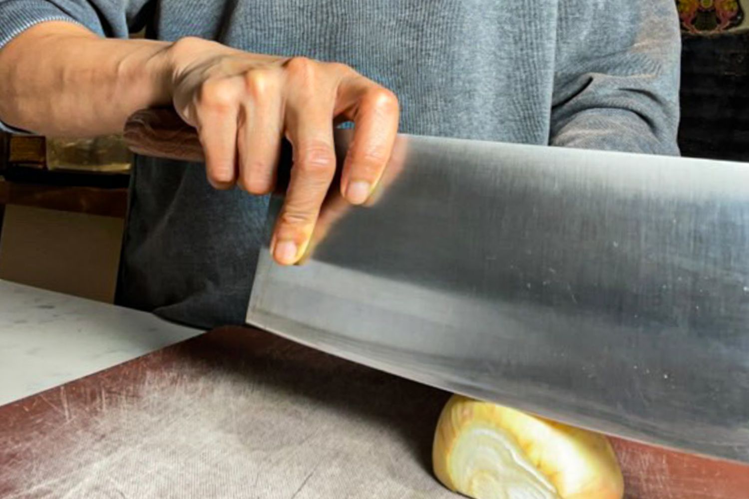 A person slicing an onion with a large knife on a cutting board